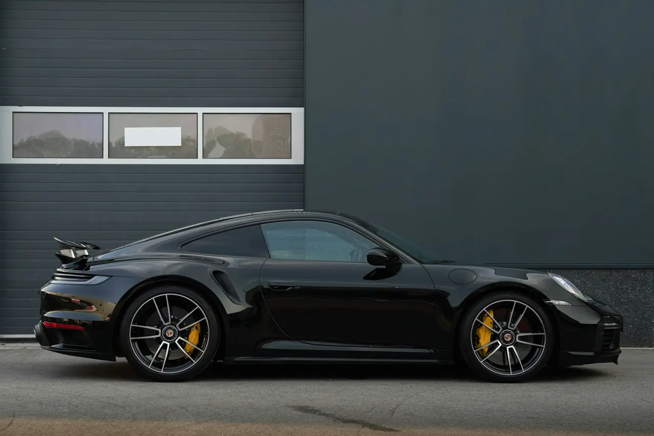 Porsche 911 Turbo nera, vista laterale davanti a un capannone grigio